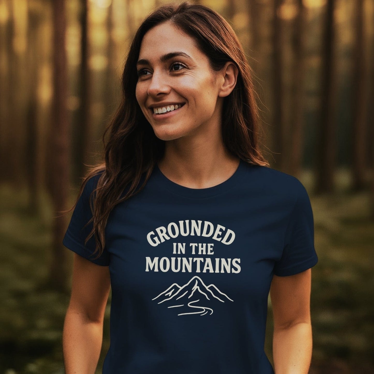 Woman in forest wearing Grounded In The Mountains T-shirt with mountain design, embodying adventure-ready comfort and durability for outdoor enthusiasts.