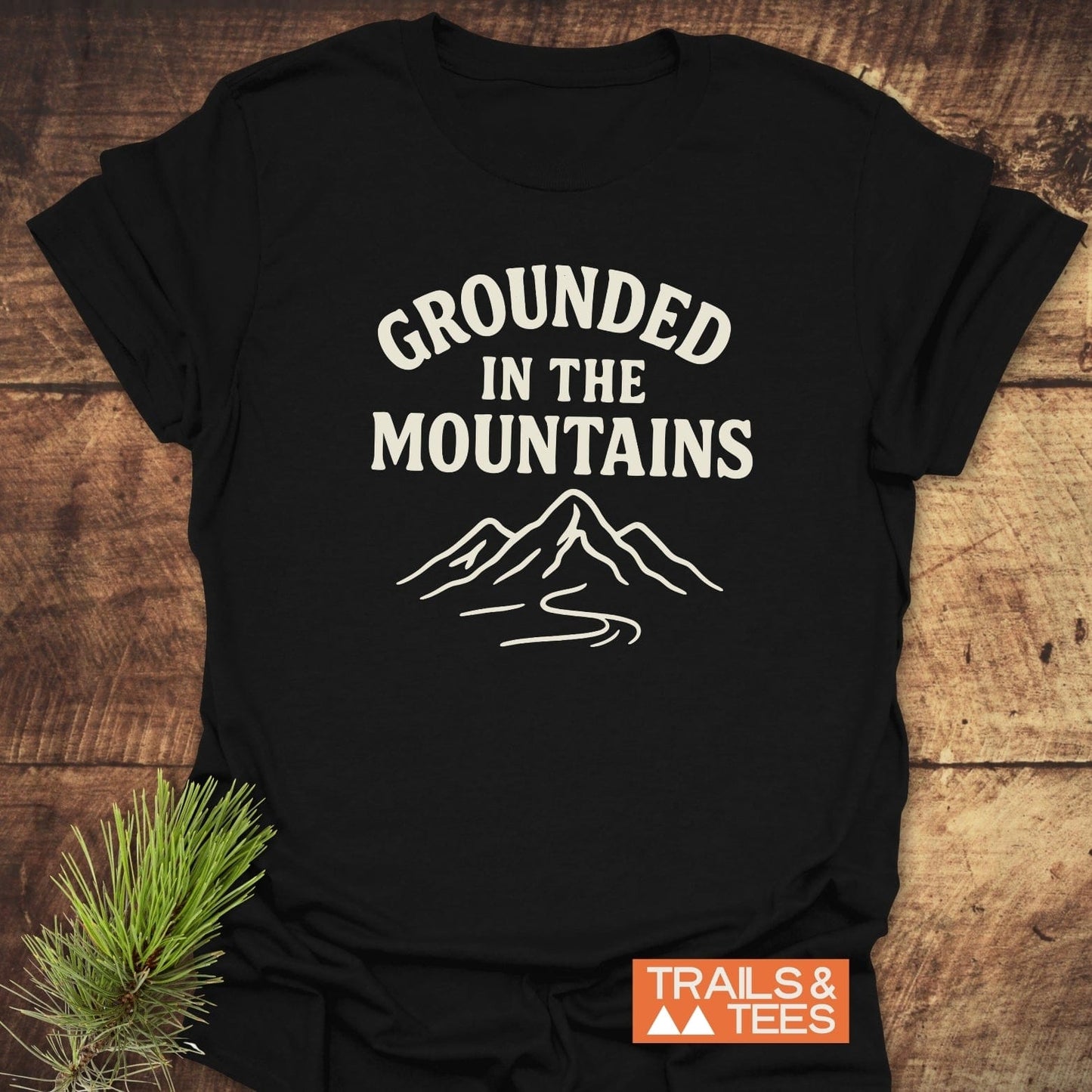 Grounded In The Mountains T-Shirt featuring off-white mountain graphic on black cotton, showcasing trail inspiration with a pine sprig accent.