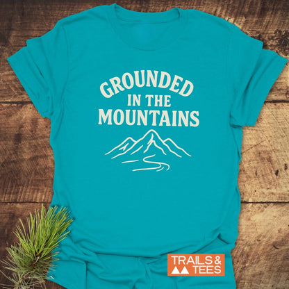 Grounded In The Mountains T-Shirt features a mountain graphic and slogan, crafted from soft cotton for comfort and durability, ideal for outdoor enthusiasts.