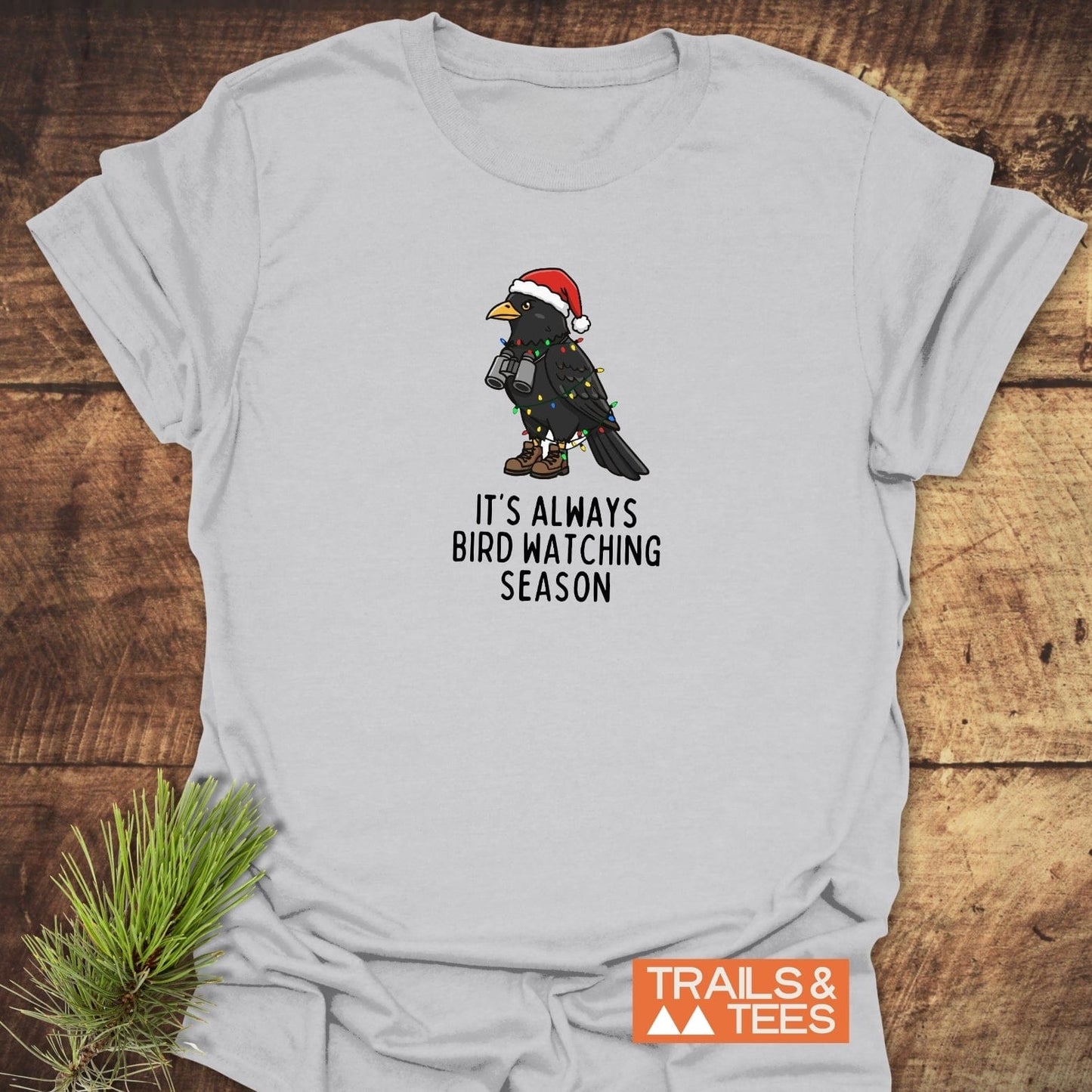 Always Bird Watching... T-Shirt: Light-gray tee with a cartoon bird in Santa hat and boots, wrapped in Christmas lights, perfect for outdoor enthusiasts.
