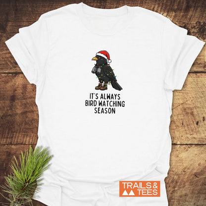 Always Bird Watching... T-Shirt featuring a cartoon bird with a Santa hat and hiking gear, wrapped in Christmas lights, on soft, durable ring-spun cotton.