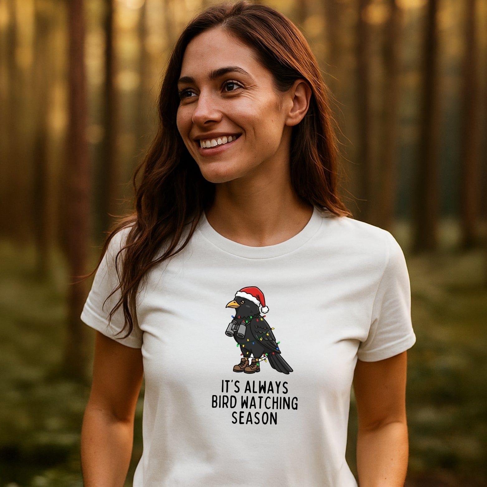Young woman in a forest wearing the Always Bird Watching... T-Shirt featuring a cartoon crow in festive attire, showcasing outdoor adventure spirit and comfort.