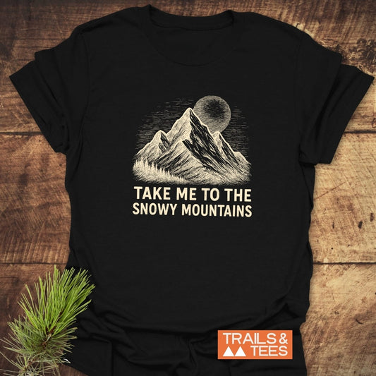 Snowy Mountains T-Shirt featuring a hand-drawn illustration of snow-capped mountains and a textured moon or sun, highlighted by the slogan TAKE ME TO THE SNOWY MOUNTAINS, on soft, lightweight cotton.