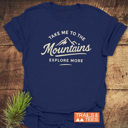 Take Me To The Mountains T-Shirt featuring a white mountain graphic and slogan, laid flat with 'Trails & Tees' logo. Made of soft, lightweight cotton, ideal for outdoor adventures.