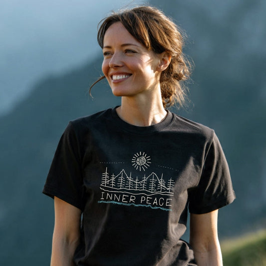 Woman wearing an Inner Peace T-Shirt featuring a line-drawing of pine trees, mountains, and sun. The tee blends comfort and adventure spirit, emphasizing outdoor appreciation with a durable, pre-shrunk design.