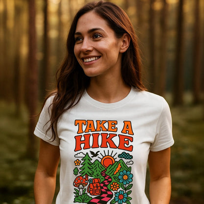 Woman in forest wearing Take A Hike Funky T-Shirt with retro outdoor scene graphic, highlighting mountains and wildflowers. The tee embodies comfort and durability, ideal for outdoor enthusiasts.