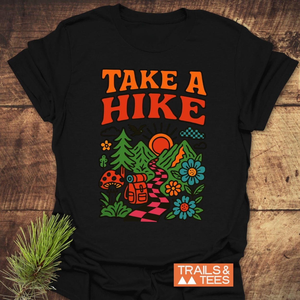 Take A Hike Funky T-Shirt featuring a retro outdoors graphic with mountains, trail, backpack, and nature elements, laid flat, showcasing its colorful design and durable print on soft cotton.
