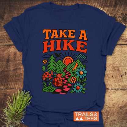 Take A Hike Funky T-Shirt featuring TAKE A HIKE slogan with vibrant hiking scene, including mountains, trees, and backpack. Logo TRAILS & TEES in corner. Perfect for outdoor enthusiasts.