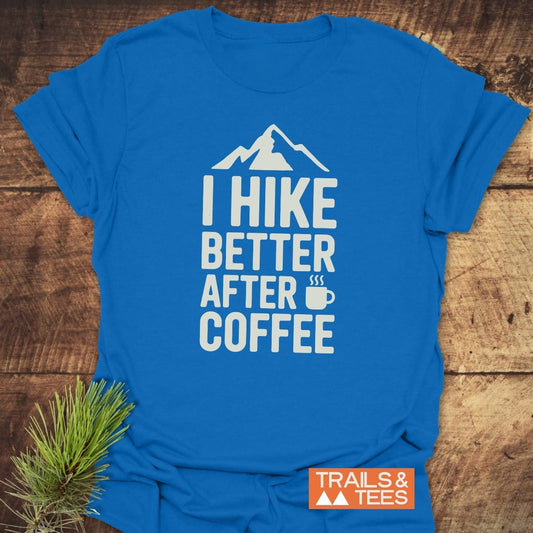 I Hike Better After Coffee T-Shirt featuring white block letters and mountain graphic, crafted from soft ring-spun cotton for comfort. Includes TRAILS & TEES label, ideal for outdoor enthusiasts.