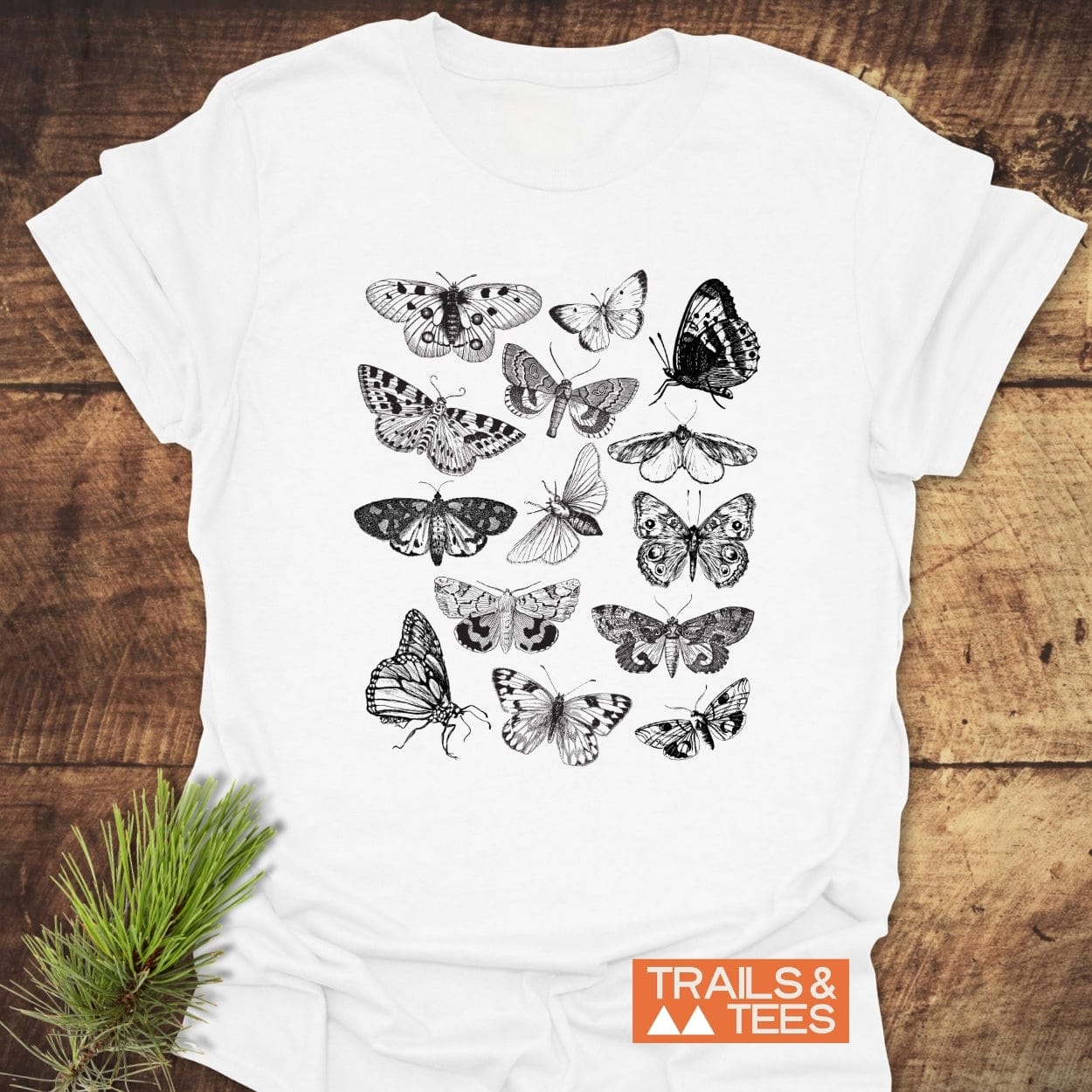 Vintage Butterfly Tattoo T-Shirt featuring a grid of vintage-style insect illustrations. Includes a “TRAILS & TEES” logo on the front, styled with a pine sprig beside it.