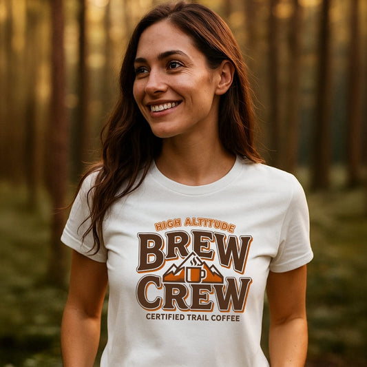 Young woman in a forest wearing a Trail Coffee T-Shirt with a mountain and mug graphic, text HIGH ALTITUDE BREW CREW, showcasing adventure-ready, soft cotton design with durable prints.