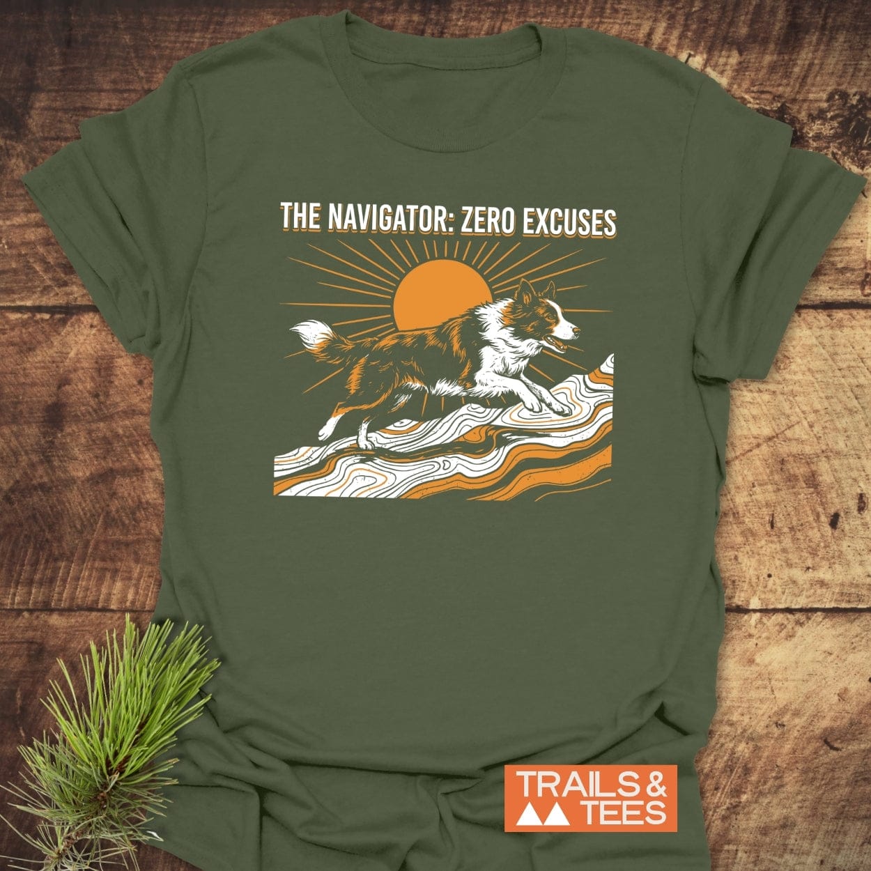 The Navigator Dog Lover T-Shirt features a border collie on contour lines with a rising sun. The slogan “ZERO EXCUSES” is above. Includes Trails & Tees logo, laid on wood.