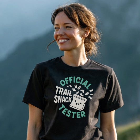 Woman wearing Official Trail Snack Tester T-shirt with a smiling snack-bag cartoon and trail mix design, highlighting soft, lightweight cotton ideal for outdoor adventures.