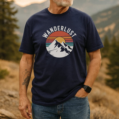 Wanderlust Retro T-Shirt on a man outdoors, showing a navy design with WANDERLUST over snow-capped peaks and a retro sunset. Paired with jeans, smartwatch, tattoo visible.