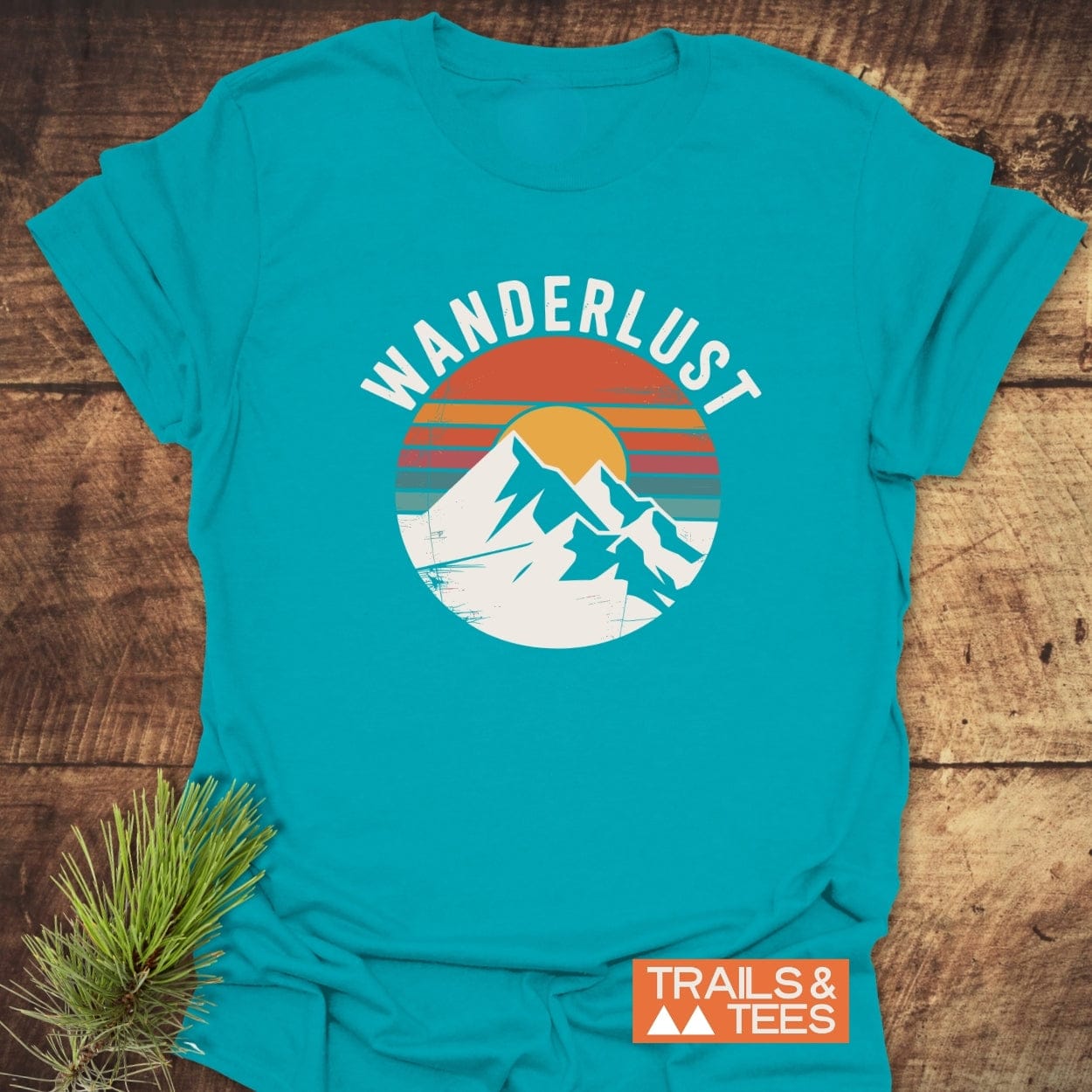 Wanderlust Retro T-Shirt with white mountain peaks and orange sun graphic. Made from soft, ring-spun cotton, it offers comfort and durability for outdoor enthusiasts. Includes “TRAILS & TEES” logo.