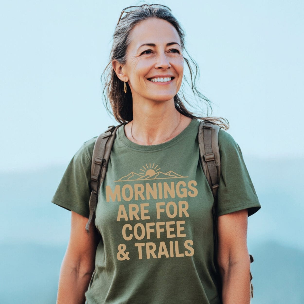 Woman outdoors wearing Morning Coffee & Trails T-Shirt, featuring a sunrise design. The tee, crafted from soft ring-spun cotton, highlights comfort and adventure, ideal for hiking and outdoor enthusiasts.