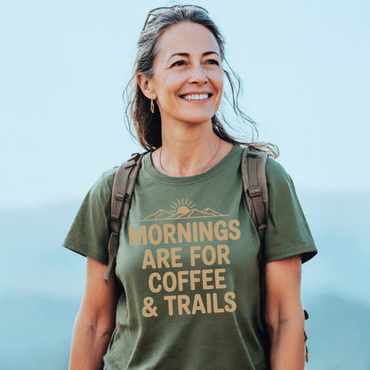 Woman outdoors wearing Morning Coffee & Trails T-Shirt, featuring a sunrise design. The tee, crafted from soft ring-spun cotton, highlights comfort and adventure, ideal for hiking and outdoor enthusiasts.