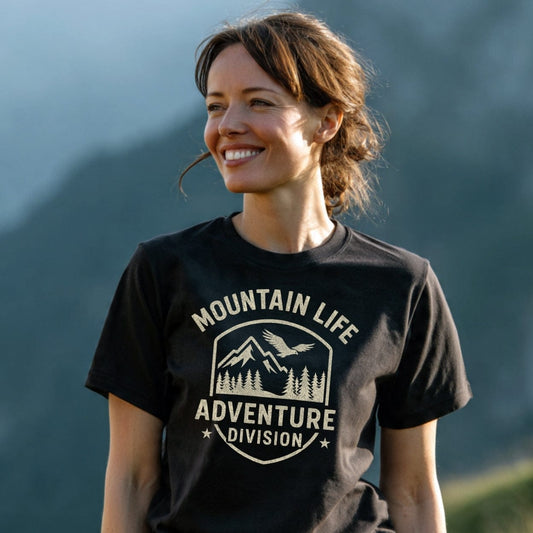 Young woman in a Mountain Life T-Shirt with crest-style graphic, standing outdoors with a mountainous backdrop, embodying outdoor adventure spirit and showcasing the tee's comfort and timeless design.