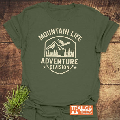 Mountain Life T-Shirt with a cream outdoor badge graphic of mountains, trees, and a bird. Features “MOUNTAIN LIFE” and “ADVENTURE DIVISION” text. Includes “TRAILS & TEES” logo, enhancing an adventurous theme.