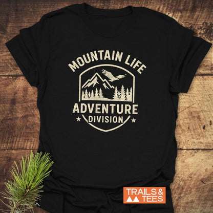 Mountain Life T-Shirt featuring a vintage-style crest with mountains, pine trees, and a soaring bird. Text reads “MOUNTAIN LIFE” and “ADVENTURE DIVISION.” Includes “TRAILS & TEES” logo.