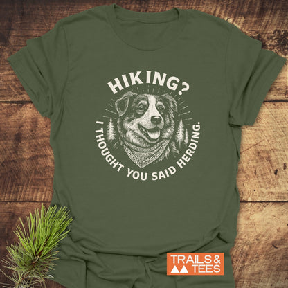 Hiking? Australian Shepherd T-Shirt with a white dog illustration and pine trees, featuring the slogan “HIKING? I THOUGHT YOU SAID HERDING.” Ideal for outdoor enthusiasts, showcasing Trail-tested comfort and design.