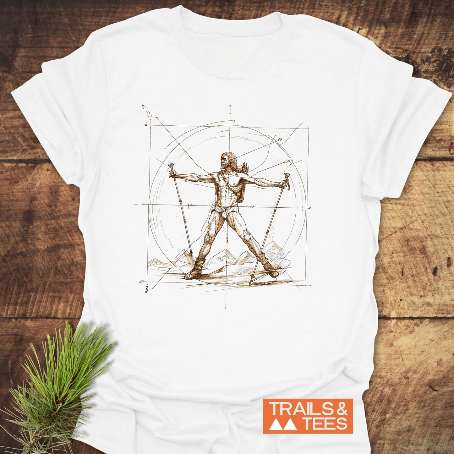 Vitruvian Hiker Da Vinci Style T-Shirt featuring a sepia sketch of a hiker with trekking poles and mountains, set against measuring lines. Trails & Tees logo visible, laid on a wooden surface.