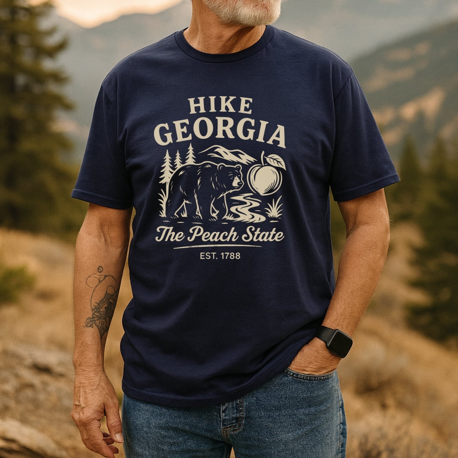 Older man wears Hike Georgia T-Shirt with HIKE GEORGIA – The Peach State and bear graphic, showcasing outdoor adventure spirit. Smartwatch visible, highlighting comfort and style in a scenic backdrop.