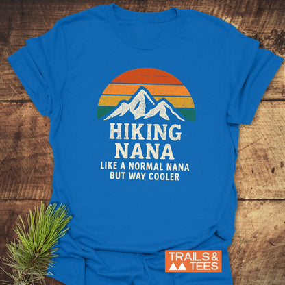 Hiking Nana Funny T-Shirt with a vintage mountain graphic and bold text, laid on a wooden surface. Features a small TRAILS & TEES logo, designed for comfort and outdoor enthusiasts.