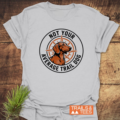 Not Your Average Trail Dog Wiener T-Shirt featuring a brown trail dog logo on a light-gray shirt. It showcases a compass rose design with the phrase encircling the image, embodying outdoor adventure spirit.