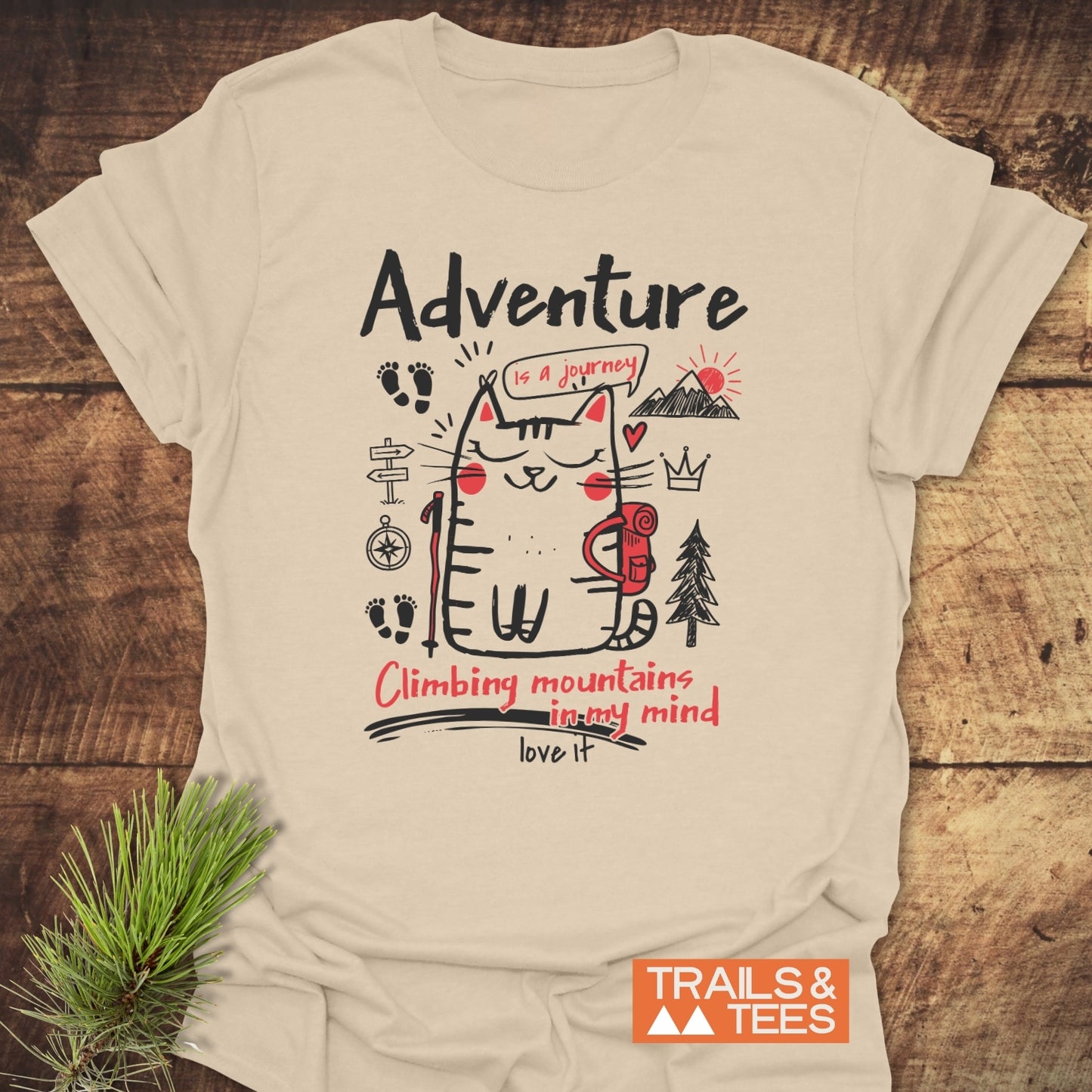 Adventure Cat Funny T-Shirt featuring a cartoon cat with a backpack, trekking pole, and mountain doodles. It says Adventure is a journey and Climbing mountains in my mind. Love it.