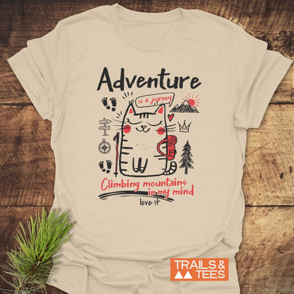 Adventure Cat Funny T-Shirt featuring a cartoon cat with a backpack, trekking pole, and mountain doodles. It says Adventure is a journey and Climbing mountains in my mind. Love it.