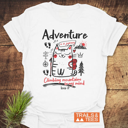 Adventure Cat Funny T-Shirt featuring a cartoon cat with a backpack and doodles like a trail signpost, compass rose, and mountain. Includes phrases Adventure is a journey and Climbing mountains in my mind.