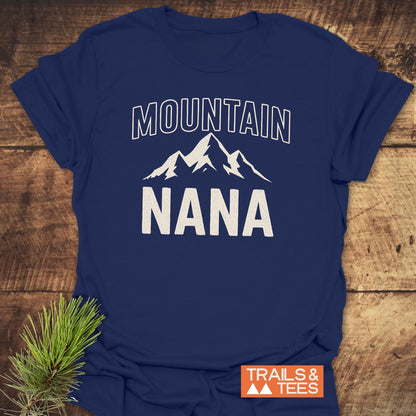 Mountain Nana T-Shirt features a white mountain peak graphic with MOUNTAIN NANA text on soft navy-blue cotton, highlighting outdoor spirit. Includes Trails & Tees logo and pine sprig accent.