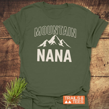 Mountain Nana T-Shirt featuring a stylized mountain graphic with MOUNTAIN above and NANA below, laid flat with a pine sprig beside it, showcasing its trail-tested comfort and timeless design.