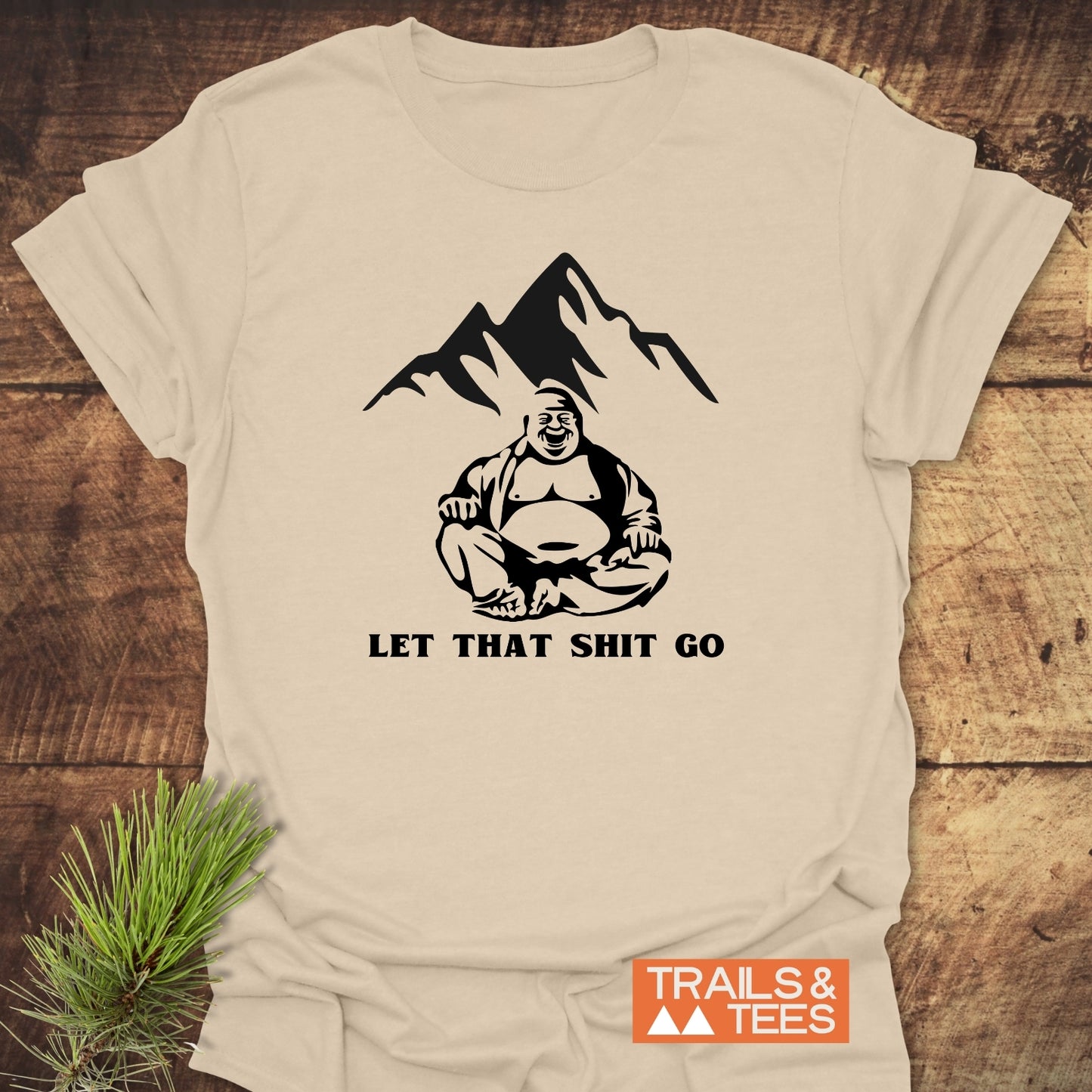 Let That Sh*t Go Funny T-Shirt featuring a laughing Buddha graphic with mountain peaks. Made from lightweight cotton for comfort, it showcases a bold slogan, perfect for outdoor enthusiasts.