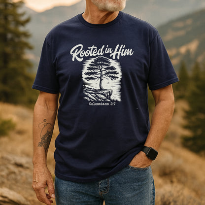 Man outdoors in a Rooted In Him Mountain T-Shirt, featuring a stylized tree and Colossians 2:7. Paired with jeans, he exudes adventure-ready comfort and timeless design.