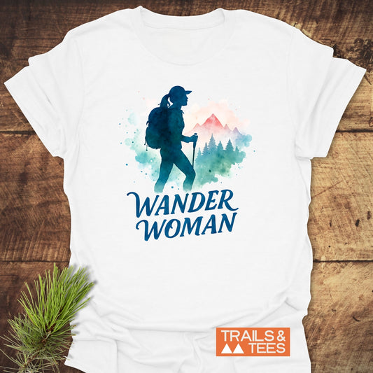 Wander Woman Watercolor T-Shirt featuring a watercolor-style woman hiker silhouette with pine trees and a mountain, slogan WANDER WOMAN, and TRAILS & TEES logo on a soft white cotton shirt.