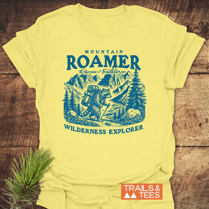 Mountain Roamer Raccoon T-Shirt featuring a playful raccoon graphic with hiking gear, surrounded by a mountain-forest scene. Accentuated by Raccoon Trailblazer and Wilderness Explorer text, perfect for outdoor enthusiasts.
