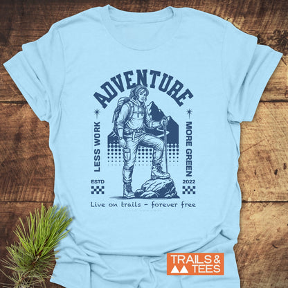 Adventure Retro T-Shirt on wooden surface, features a backpacker illustration with ADVENTURE above. Phrases LESS WORK, MORE GREEN and Live on trails – forever free complete the design.