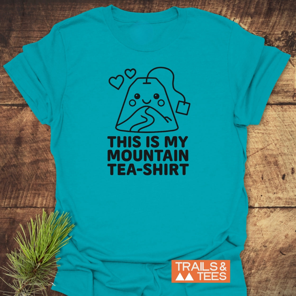 The Mountain Tea Shirt T-Shirt features a smiling tea bag design with a trail and hearts, paired with the slogan THIS IS MY MOUNTAIN TEA-SHIRT, embodying outdoor adventure spirit.
