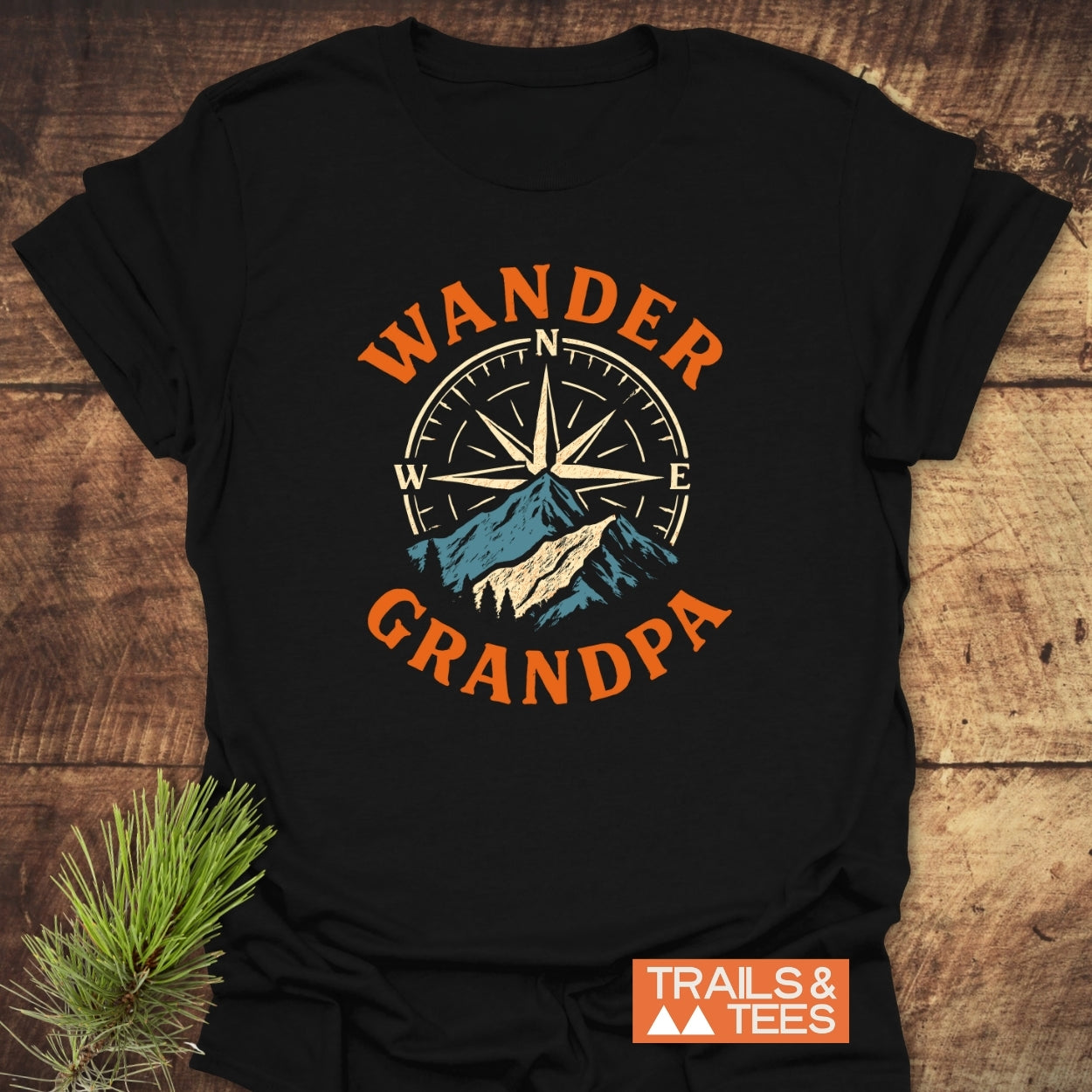 Wander Grandpa T-Shirt flat-lay featuring a compass rose and mountain design. Crafted from soft, ring-spun cotton for comfort, it showcases orange lettering and a durable print by Trails & Tees.