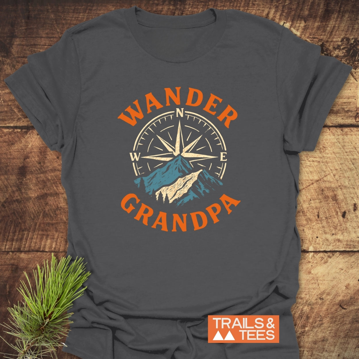 Wander Grandpa T-Shirt featuring a compass rose and mountains graphic. Made from soft ring-spun cotton, perfect for outdoor enthusiasts. Includes “TRAILS & TEES” logo; spruce branch as a prop.
