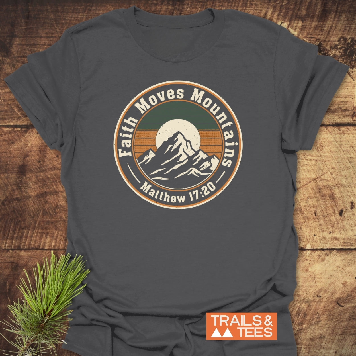 Faith Moves Mountains T-Shirt with a vintage mountain graphic and motivational quote. Laid flat on rustic wood, showcasing its soft, lightweight cotton fabric. Perfect for outdoor enthusiasts and everyday adventure.