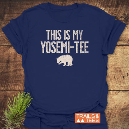 Navy-blue This Is My Yosemi-Tee Funny T-Shirt with distressed white text and bear silhouette, displayed on wood. Featuring TRAILS & TEES logo, styled with a pine sprig for an outdoorsy feel.