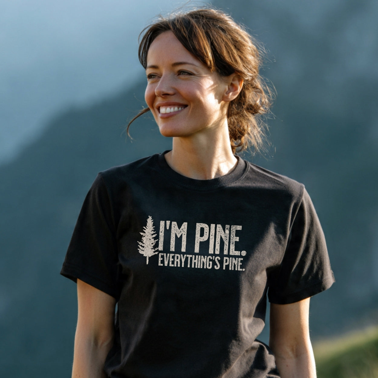 Woman outdoors wearing “I'M PINE. EVERYTHING'S PINE.” T-shirt with a stylized pine tree, highlighting trail-tested comfort, soft cotton, durable print, and eco-friendly design for outdoor enthusiasts.
