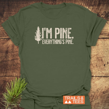 I'm Pine. Everything's Pine. T-Shirt featuring a pine-tree silhouette and slogan, crafted from soft, lightweight cotton. Seen with a pine branch on wood, representing outdoor adventure and comfort.