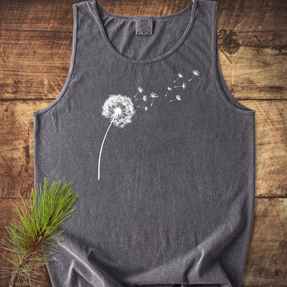 Dandelion Comfort Colors 9360 Tank Top, charcoal-gray, with a white dandelion design. Laid flat on wood, showcasing its relaxed fit and sustainable US cotton construction.