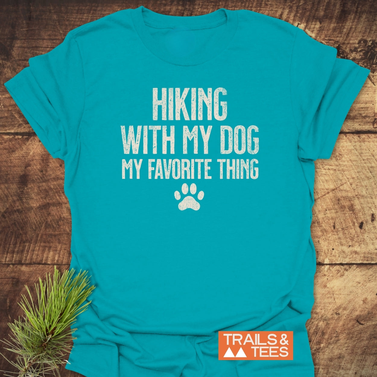 Hiking With My Dog T-Shirt features distressed white text and a paw-print on teal fabric, laid flat. Part of Trails & Tees, designed for comfort and outdoor enthusiasts.