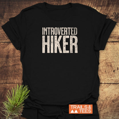 Black Introverted Hiker T-shirt with distressed white text, styled with a pine sprig. Features soft ring-spun cotton, durable print, taped shoulders, and no side seams. Includes TRAILS & TEES logo.