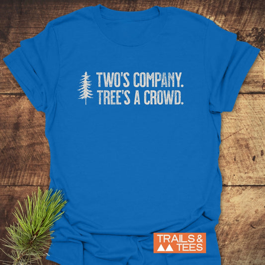 Two's Company Funny T-Shirt features a distressed white pine tree and witty text on a bright blue short-sleeve design, laid on rustic wood. Perfect for outdoor enthusiasts seeking comfort and style.